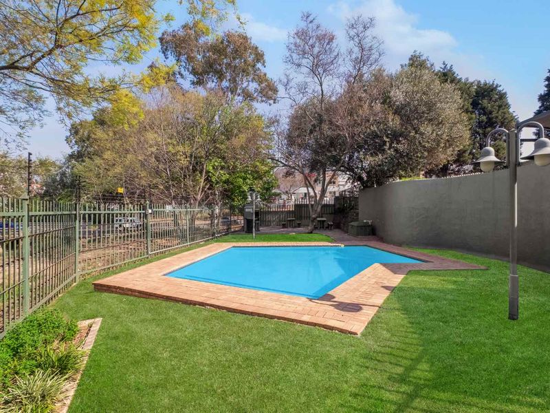 A well-maintained outdoor pool area featuring a swimming pool with brick coping, surrounded by a manicured lawn and secure perimeter fencing.