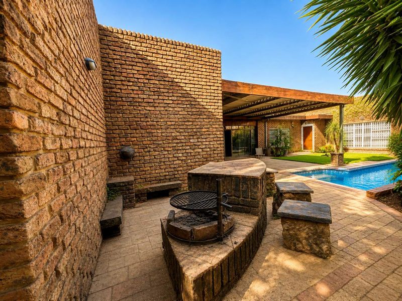 Outdoor entertainment area featuring a built-in braai, covered patio, and swimming pool set within a private courtyard with exposed brick finishes.