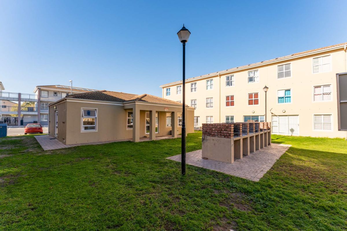 Communal outdoor area featuring a brick-built barbecue station, paved patio space, and landscaped lawn situated between residential apartment blocks.