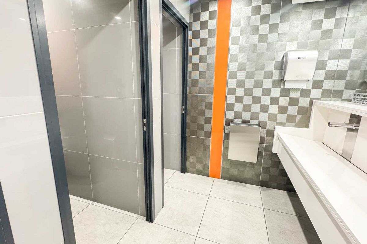 Modern office bathroom featuring tiled walls and flooring, an integrated washbasin with sensor-operated tap, and wall-mounted paper towel dispenser.