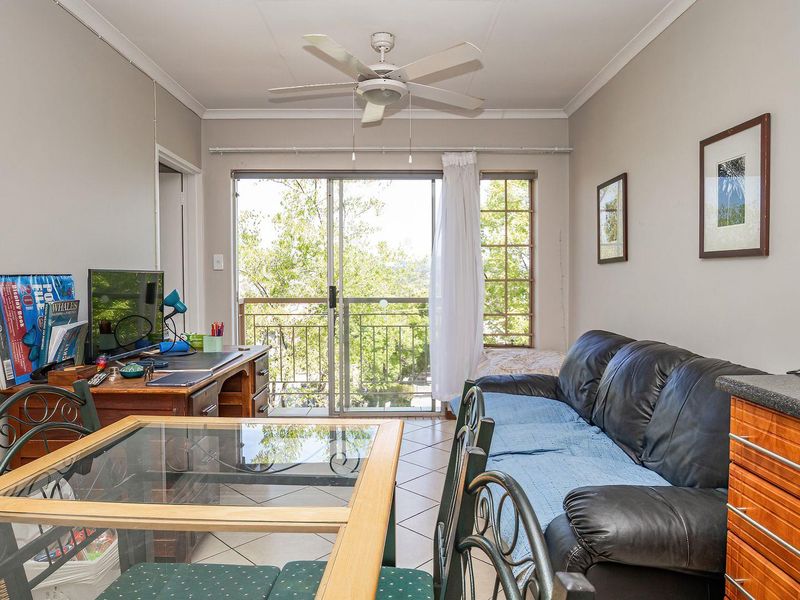 Open plan living and kitchen area featuring tiled floors, a ceiling fan, and sliding glass doors leading to a balcony with natural light.