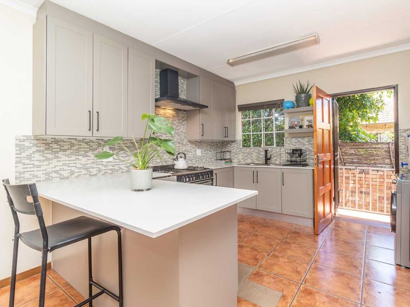 Modern kitchen featuring neutral cabinetry, gas hob, extractor fan, tiled backsplash, and a breakfast bar, with direct access to an outdoor area.