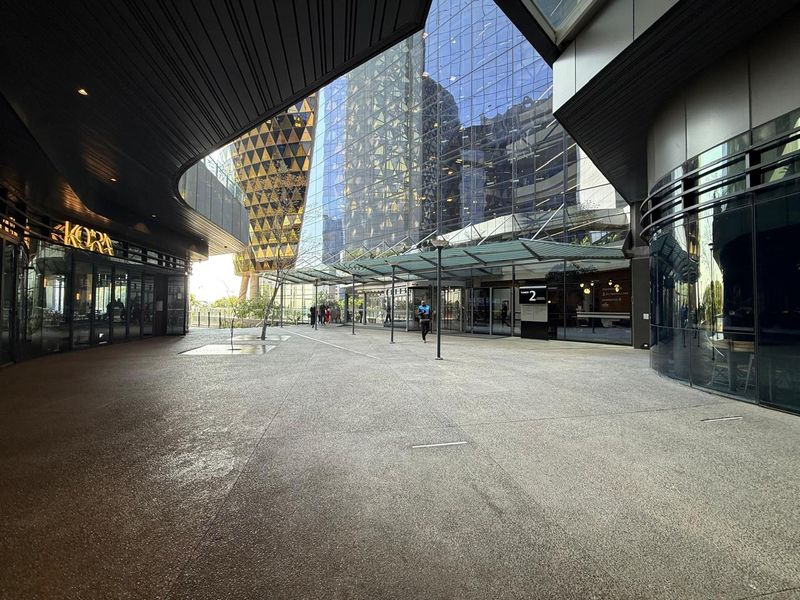 Modern commercial office complex entrance featuring a covered pedestrian plaza, glass facade, and contemporary architectural design.