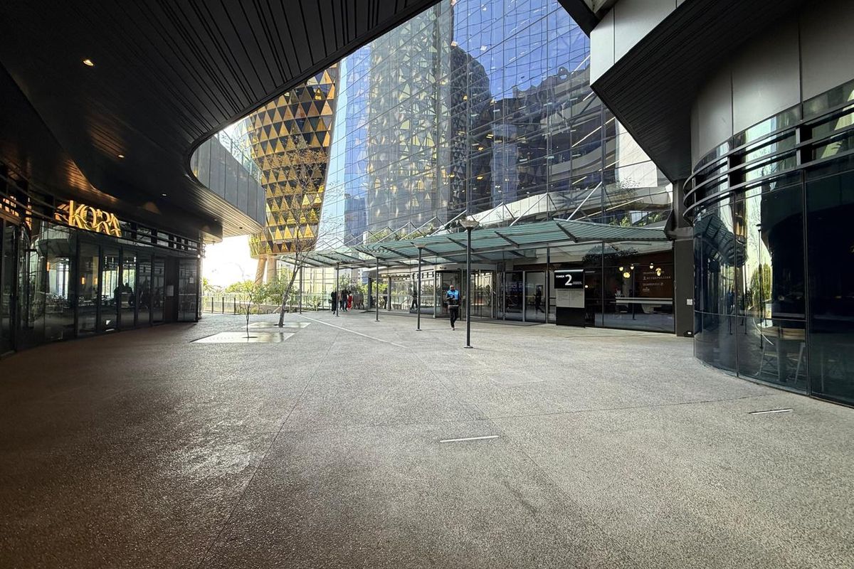 Modern commercial office complex entrance featuring a covered pedestrian plaza, glass facade, and contemporary architectural design.