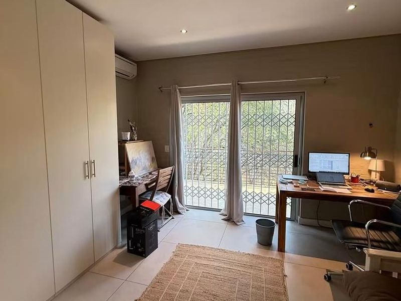 A functional bedroom featuring built-in cupboards, tiled flooring, air conditioning, and a sliding door with security gate providing access to the outdoors.