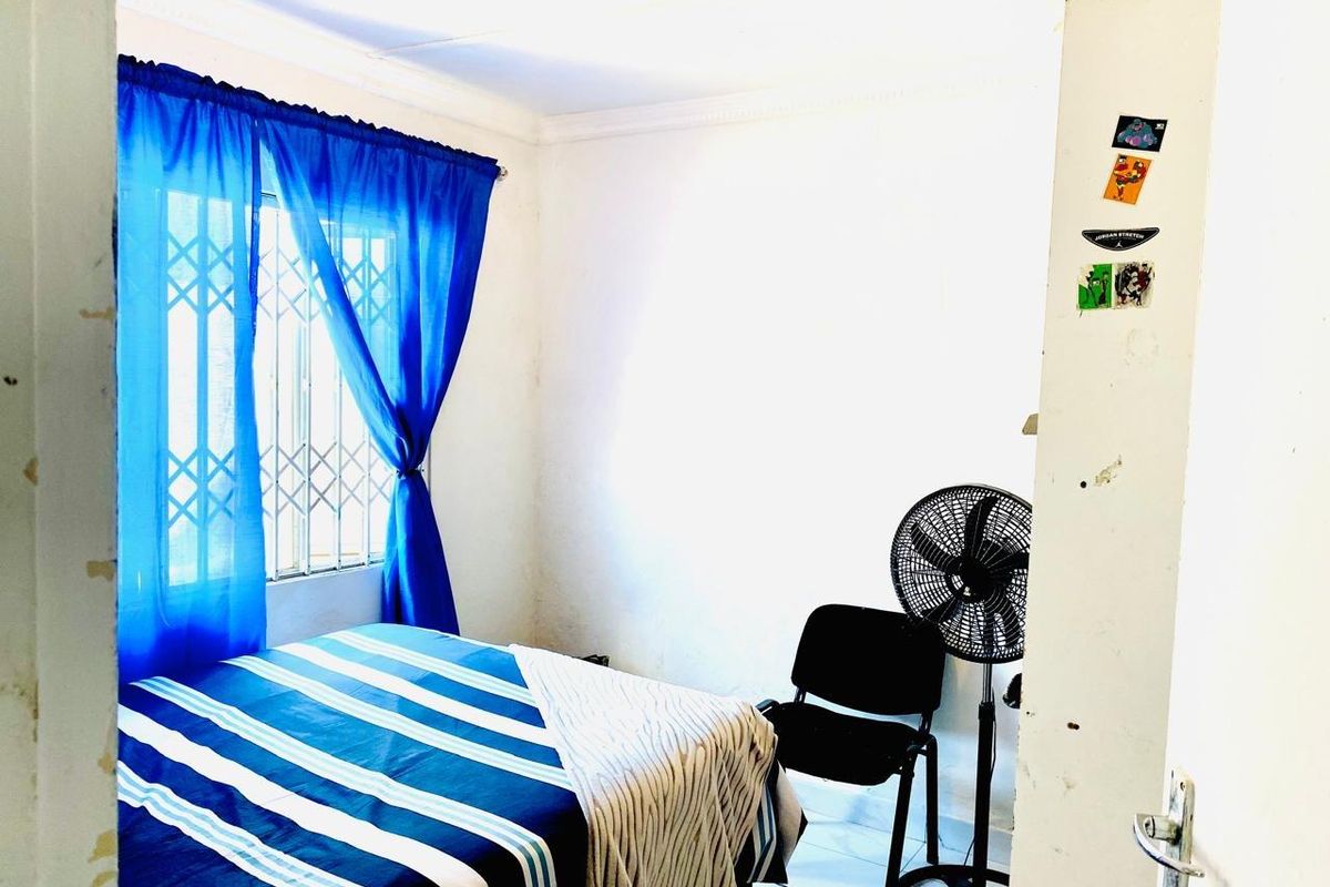 A compact bedroom featuring tiled flooring, a window with a security gate, and basic finishes, offering a functional space for rest.