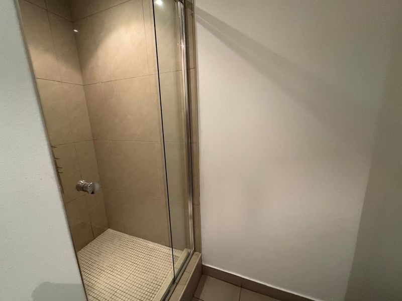 A clean, modern bathroom shower featuring a glass enclosure, neutral wall tiling, and mosaic floor tiles.