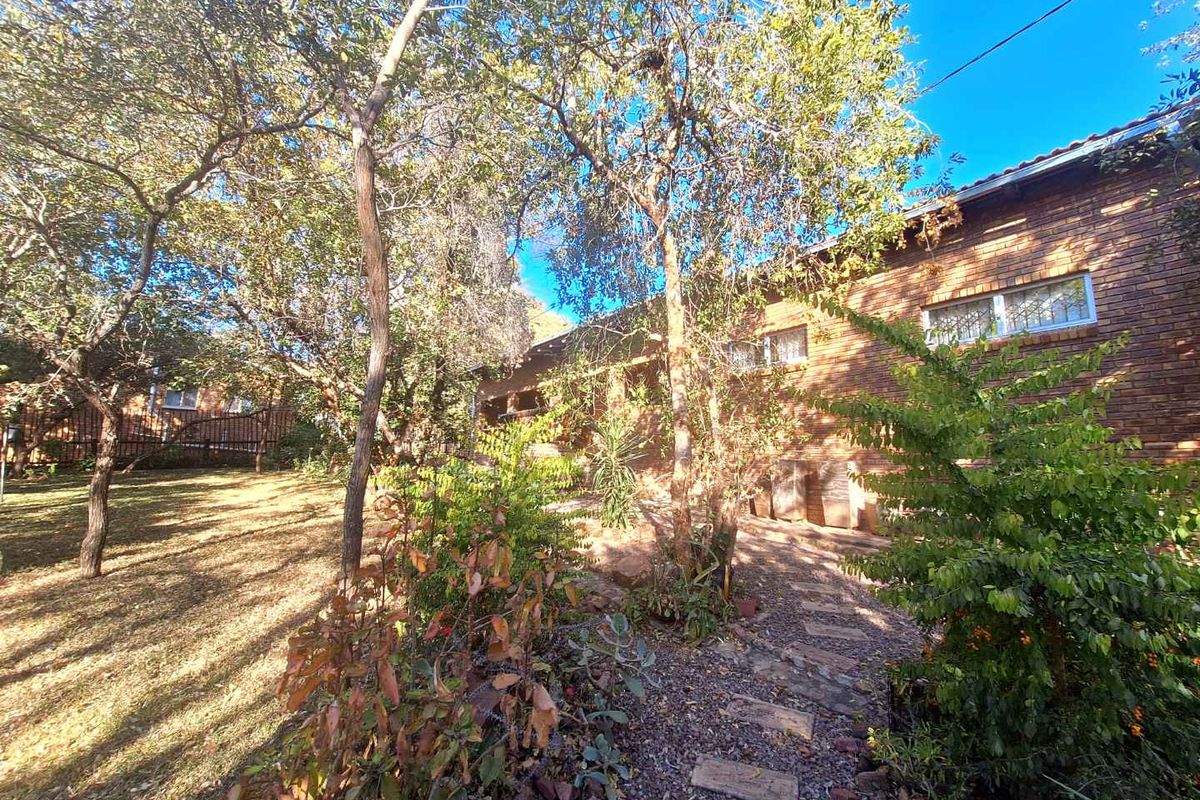A view of the rear exterior of the brick house, featuring a landscaped garden with mature trees and a stone pathway.