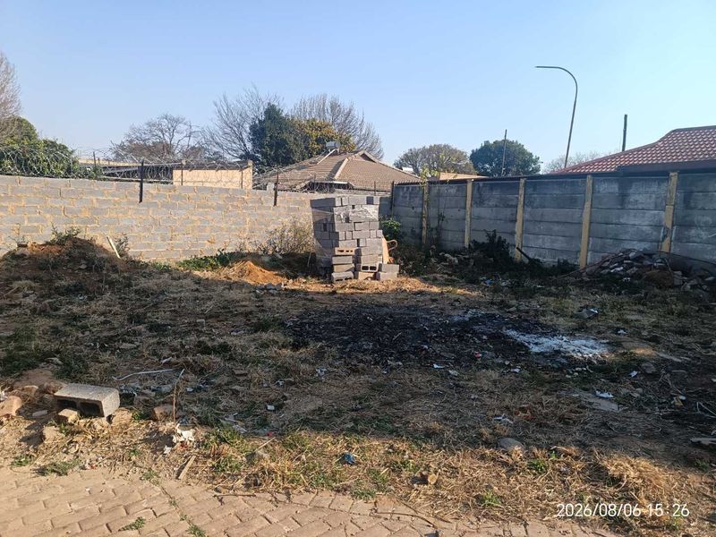 A vacant residential plot featuring perimeter walling with razor wire and some existing paving, requiring clearing and landscaping.