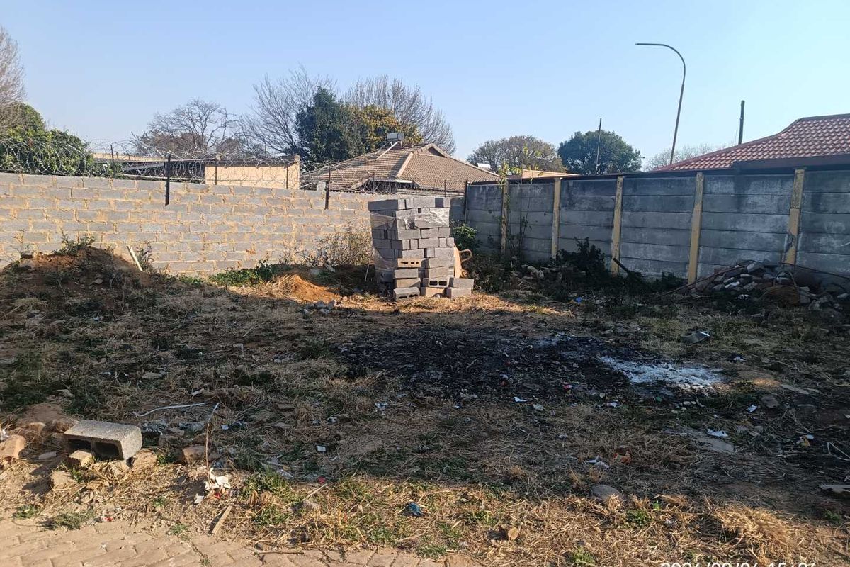 A vacant residential plot featuring perimeter walling with razor wire and some existing paving, requiring clearing and landscaping.