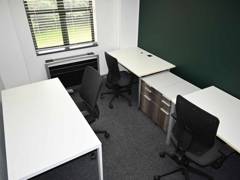 A functional office space featuring carpeted flooring, an integrated HVAC unit, and large windows with blinds, providing a professional work environment.