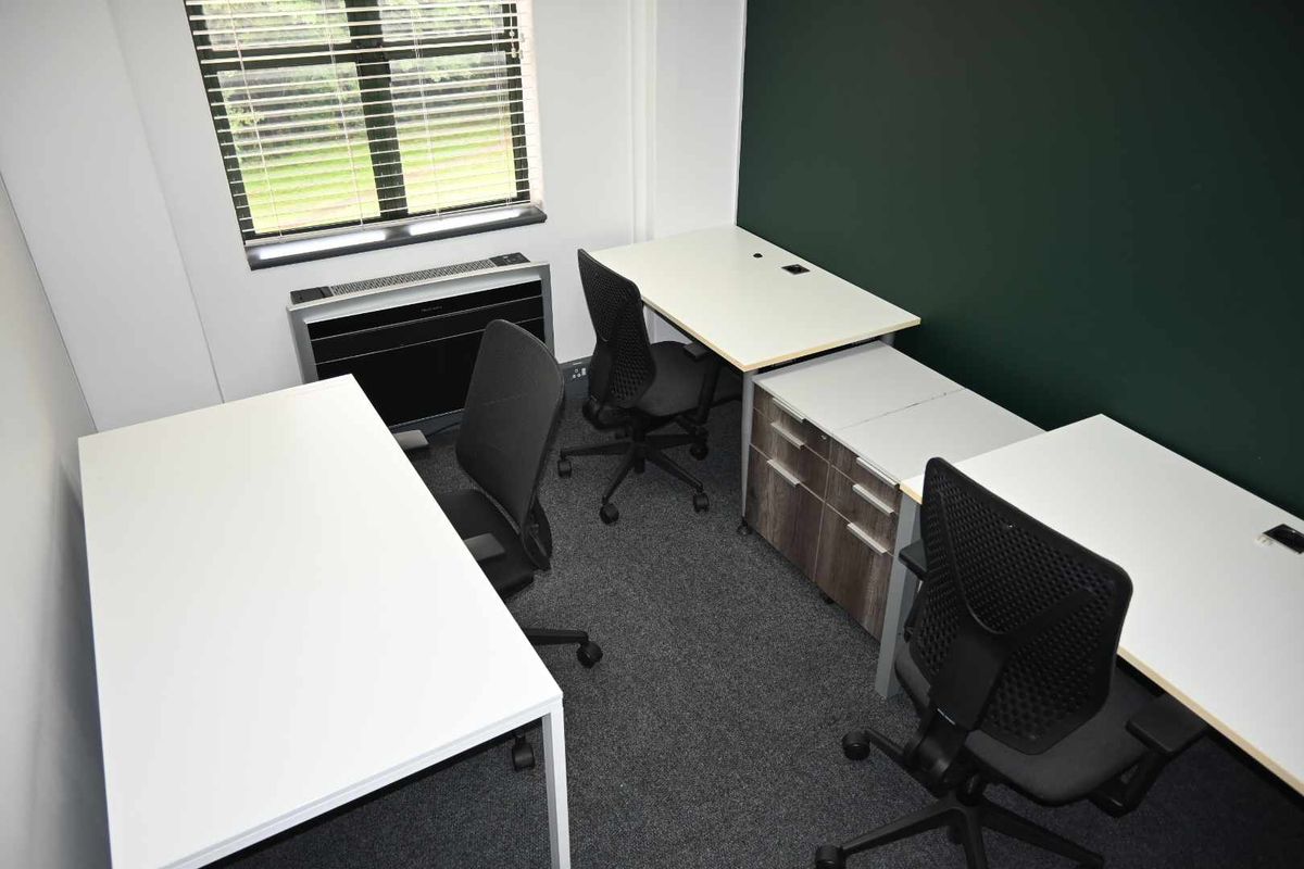 A functional office space featuring carpeted flooring, an integrated HVAC unit, and large windows with blinds, providing a professional work environment.