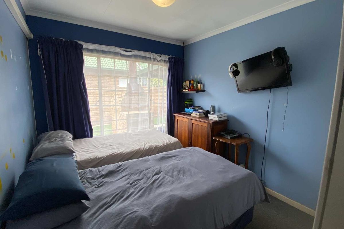A bedroom featuring blue walls, carpeted flooring, and a large window with views of the exterior brick wall.