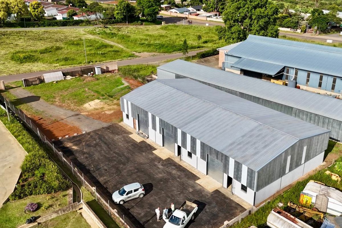 Aerial view of an industrial property featuring multiple warehouse units with corrugated metal roofing, paved yard space, and secure perimeter fencing.