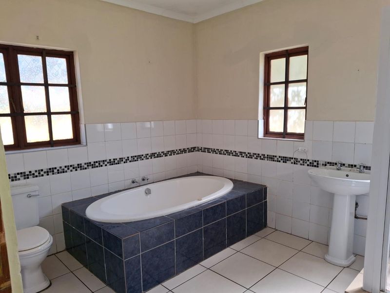 A functional bathroom featuring a built-in bathtub, pedestal sink, and toilet, finished with tiled splashbacks and timber-framed windows.