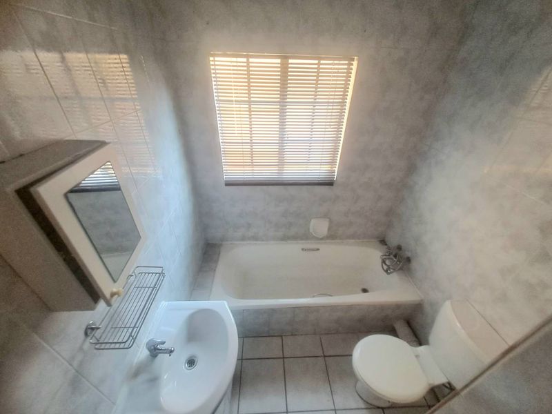 A functional bathroom featuring a bathtub, pedestal basin, toilet, and tiled finishes, offering a clean and practical space.