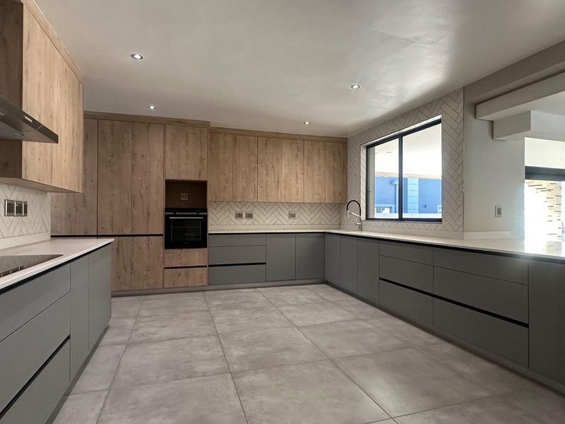 A modern, spacious kitchen featuring two-tone cabinetry, quartz countertops, a herringbone tile backsplash, built-in oven, and large format floor tiles.