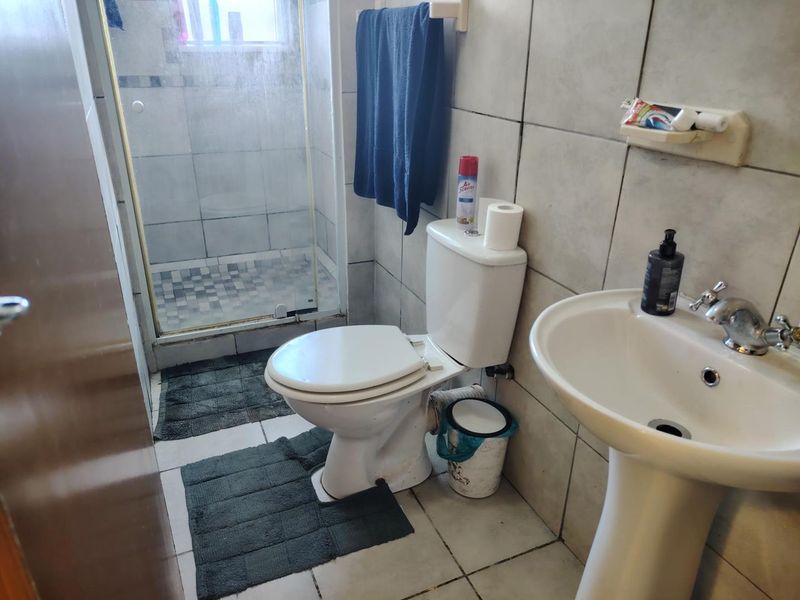 A compact bathroom featuring a pedestal basin, toilet, and a glass-enclosed shower with tiled finishes throughout.