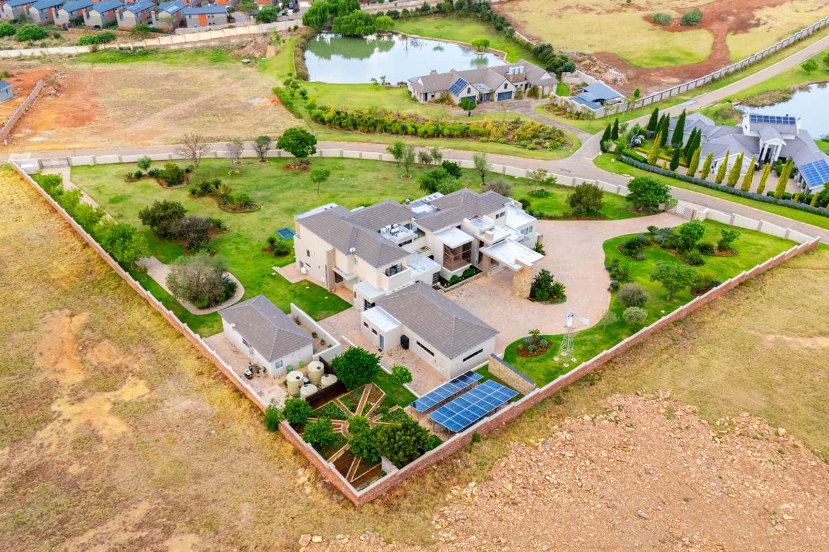 Aerial view of a large residential property featuring a spacious landscaped garden, paved driveway, solar panel installation, and a detached outbuilding.