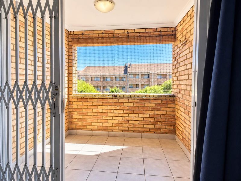 A covered balcony featuring exposed brick walls, tiled flooring, and a security gate, offering an open outlook.