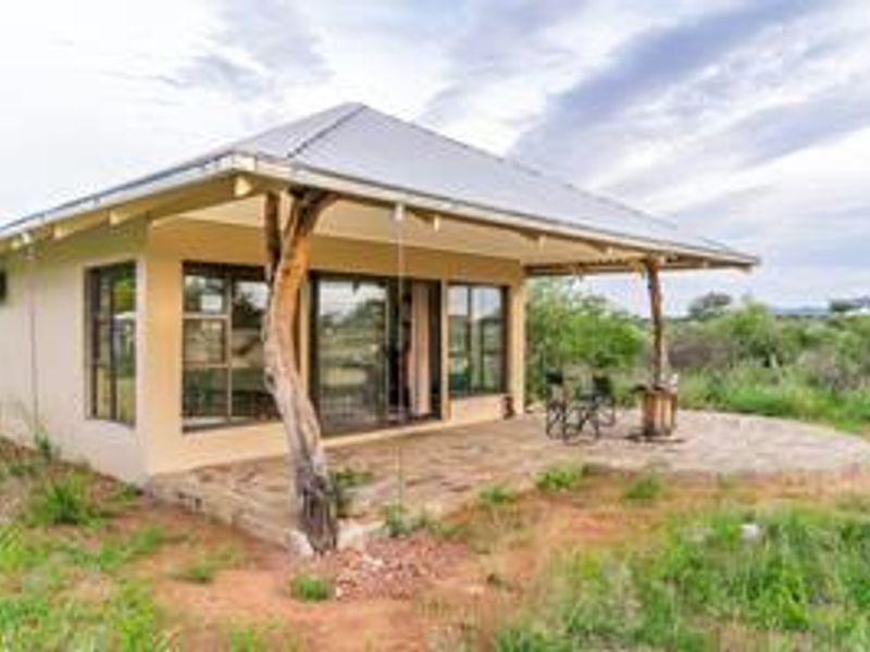A charming rural cottage featuring a covered patio with natural timber supports, metal roofing, and large glass sliding doors overlooking the surrounding landscape.