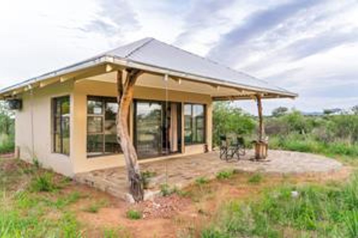 A charming rural cottage featuring a covered patio with natural timber supports, metal roofing, and large glass sliding doors overlooking the surrounding landscape.