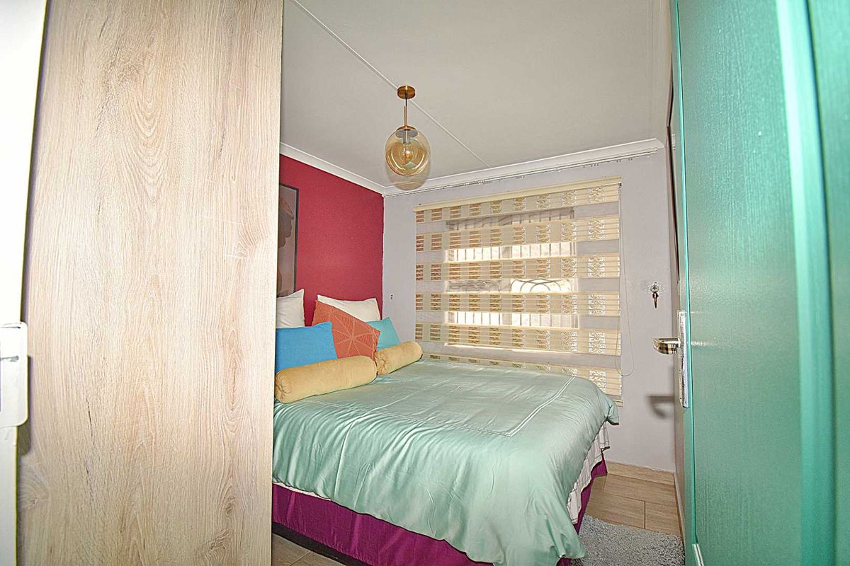 A cozy bedroom featuring a pendant light fixture, tiled flooring, and a window with fitted blinds.