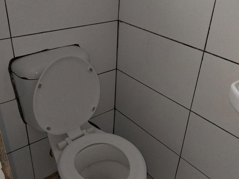 A small bathroom featuring a standard toilet with white ceramic wall and floor tiling, currently requiring maintenance and cosmetic updates.