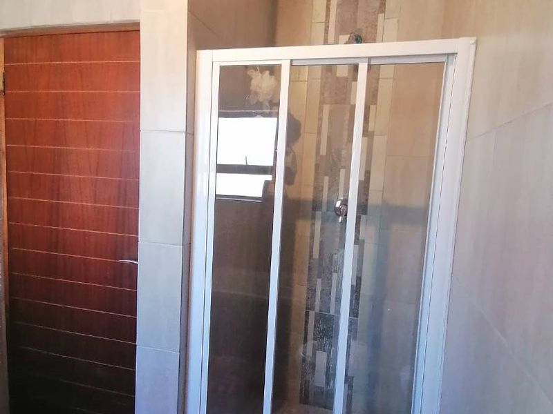 A clean bathroom featuring a glass-enclosed shower, neutral wall tiling, and a wooden door with crown molding detail.