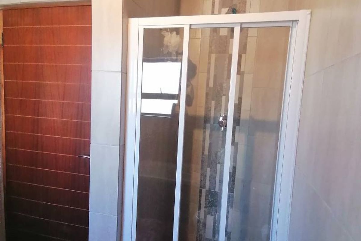 A clean bathroom featuring a glass-enclosed shower, neutral wall tiling, and a wooden door with crown molding detail.