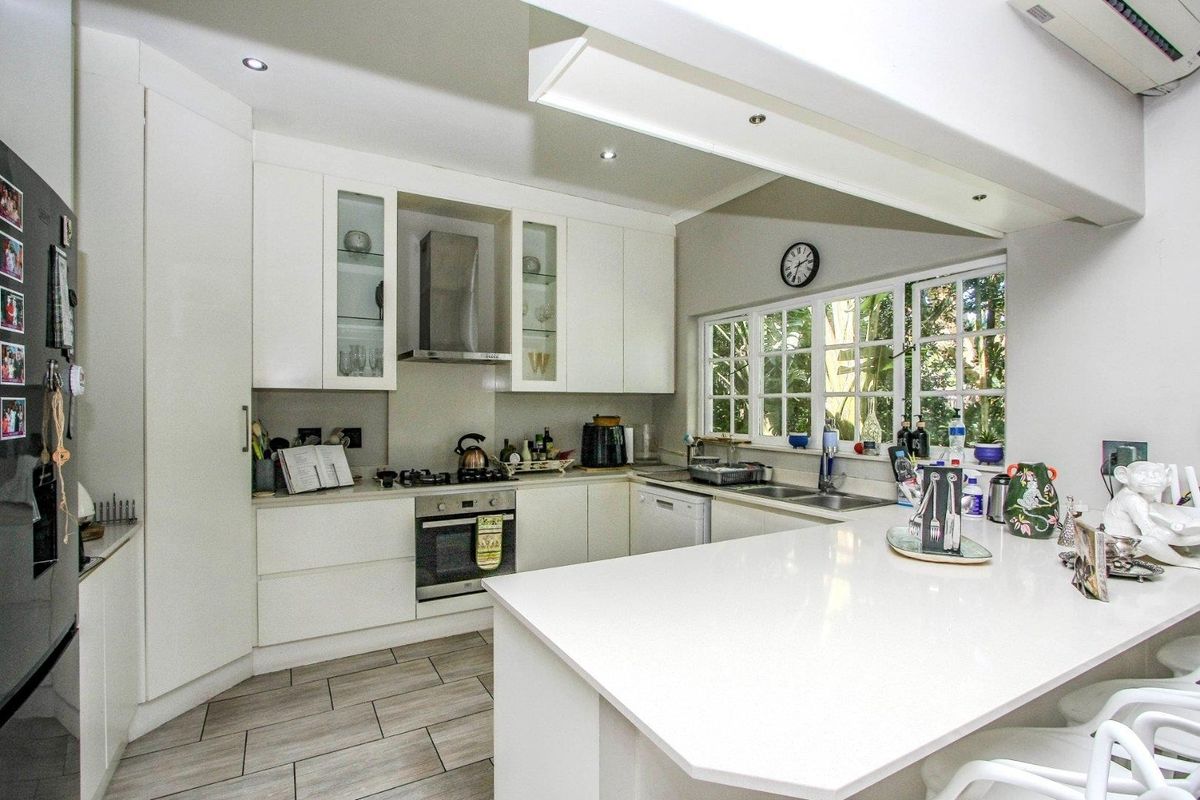 Modern kitchen featuring white cabinetry, stone countertops, integrated appliances, gas hob, and a breakfast bar, complemented by tiled flooring and ample natural light.