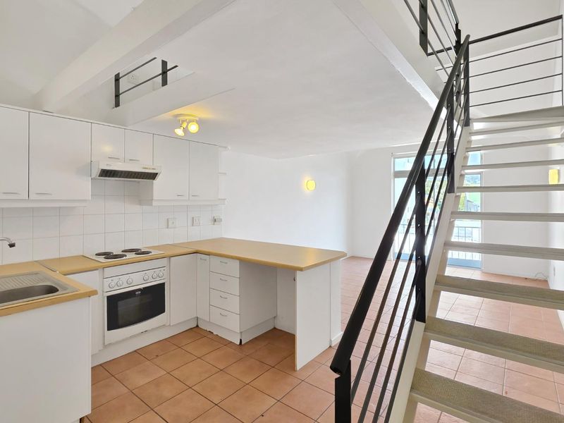 Open-plan kitchen and living area featuring tiled floors, built-in cabinetry, and a staircase leading to the upper level.