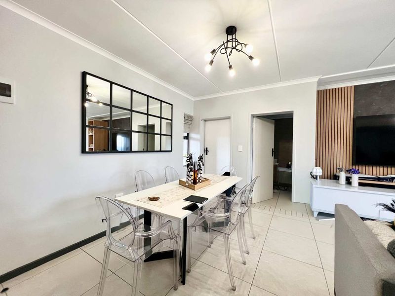 A bright dining area featuring large floor tiles, modern slatted wood wall accents, and a contemporary chandelier, creating a clean and inviting living space.