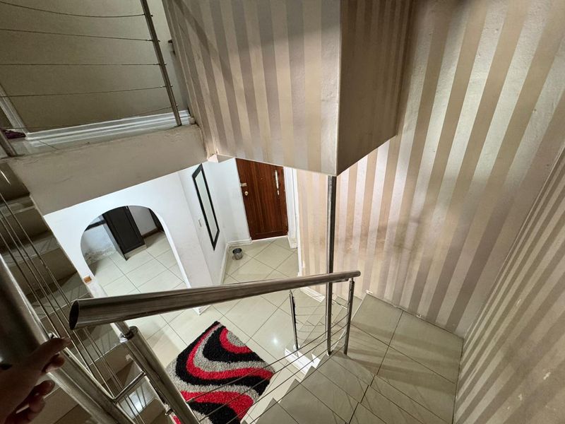 A view looking down a staircase featuring tiled flooring, a stainless steel balustrade, and striped wallpaper leading to an arched entryway.