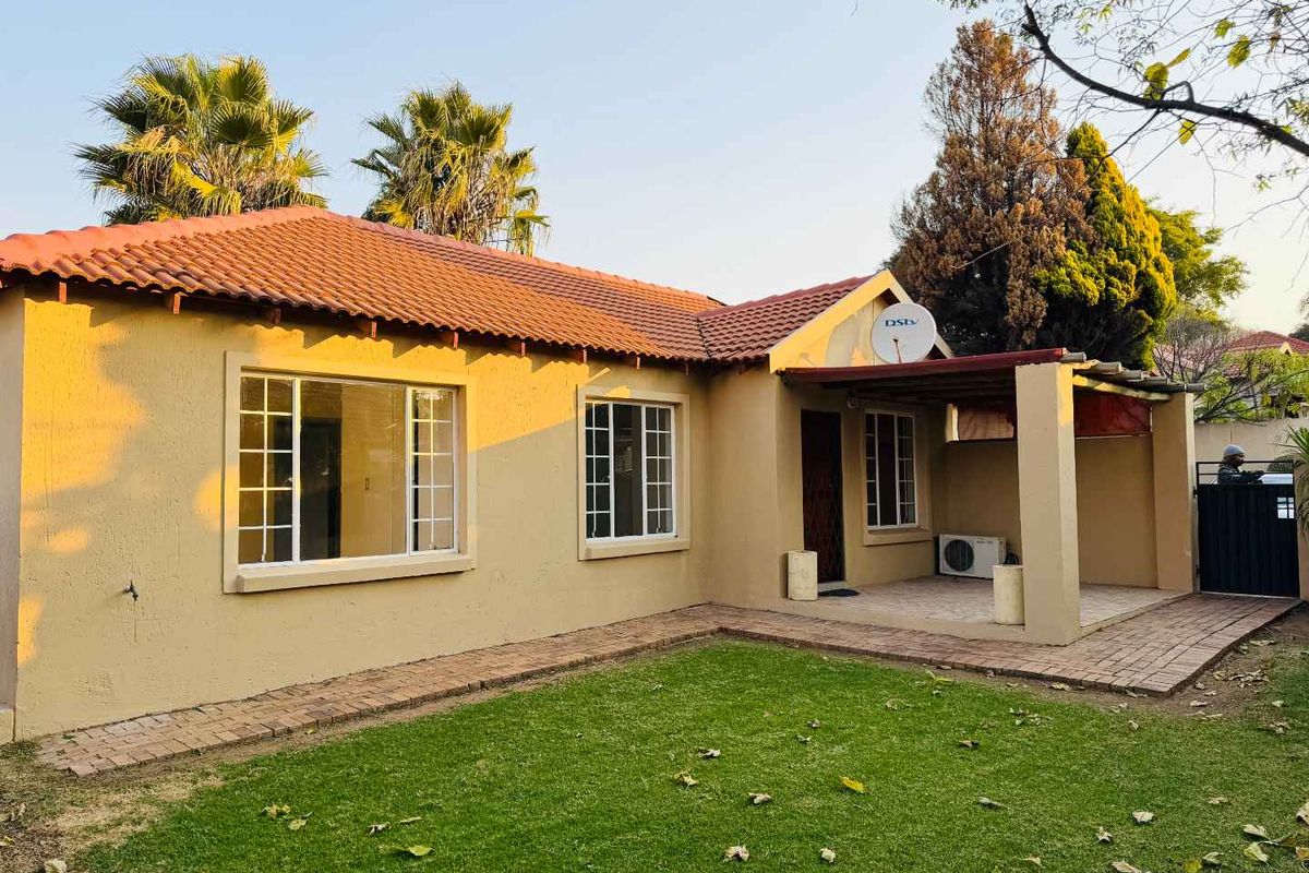 Rear view of the townhouse featuring a covered patio, paved walkway, and a private garden area with established landscaping.