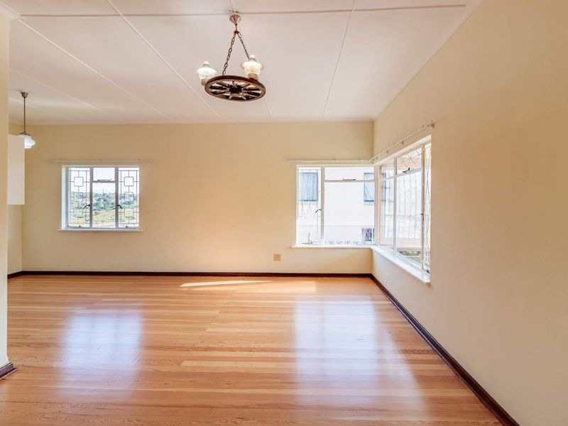 A bright and spacious living area featuring polished timber flooring, large windows providing natural light, and classic ceiling tile finishes.