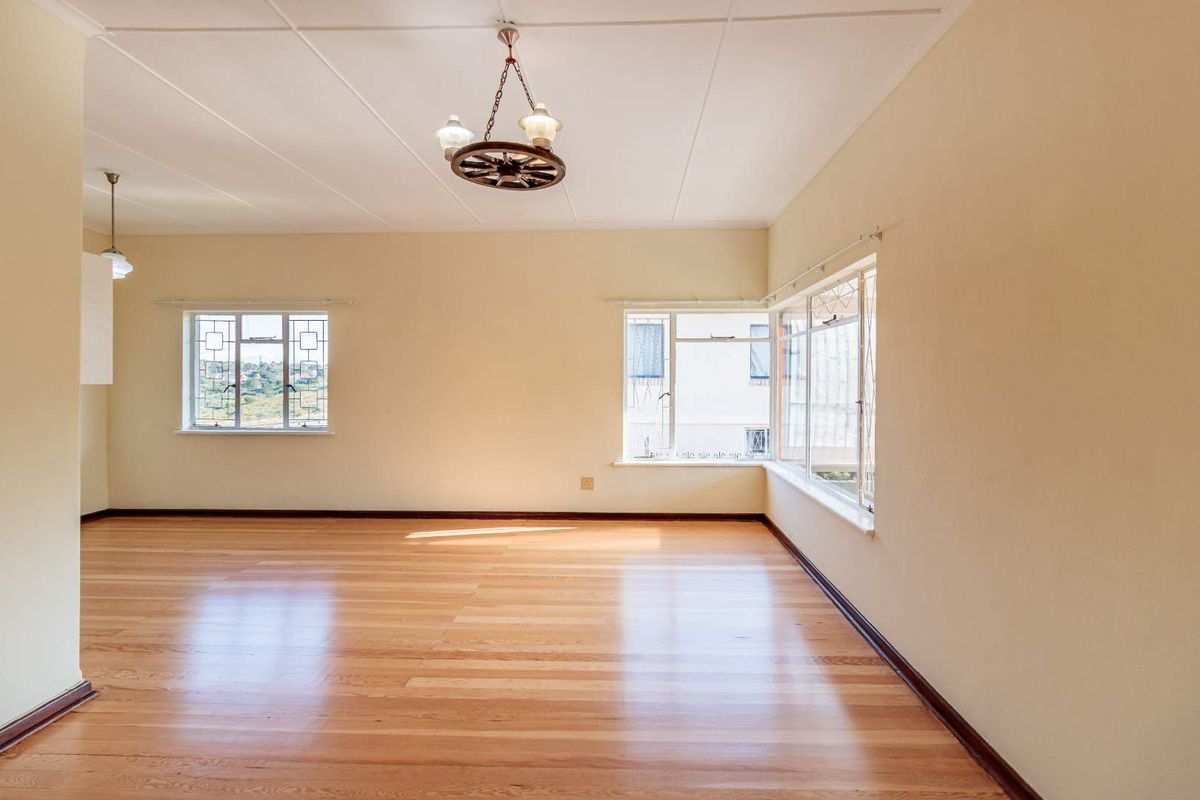 A bright and spacious living area featuring polished timber flooring, large windows providing natural light, and classic ceiling tile finishes.