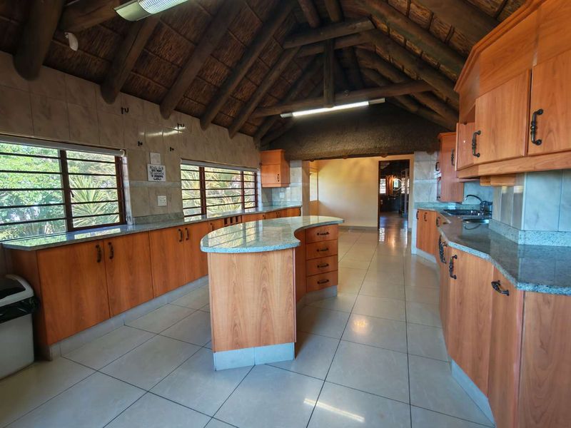 Spacious kitchen featuring wooden cabinetry, granite countertops, a central island, and a unique exposed timber thatch roof with tiled flooring throughout.