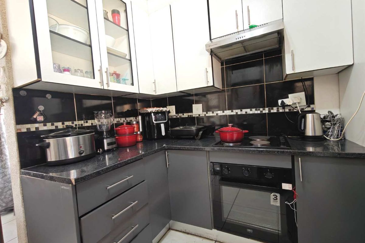 A functional kitchen featuring modern two-tone cabinetry, granite countertops, a built-in oven, and an electric hob with a tiled backsplash.