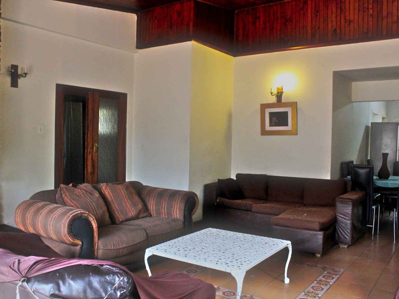 Spacious living area featuring a stone fireplace, dark timber ceiling accents, and tiled flooring, offering a warm and traditional aesthetic.