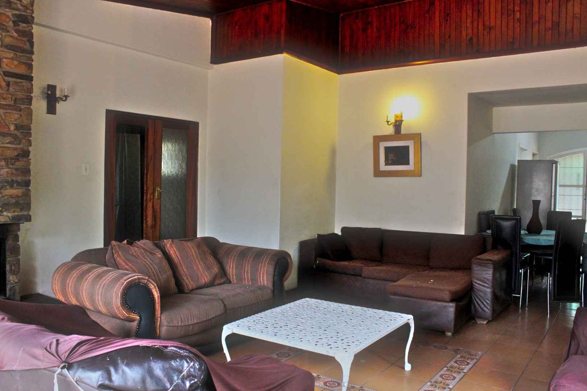 Spacious living area featuring a stone fireplace, dark timber ceiling accents, and tiled flooring, offering a warm and traditional aesthetic.