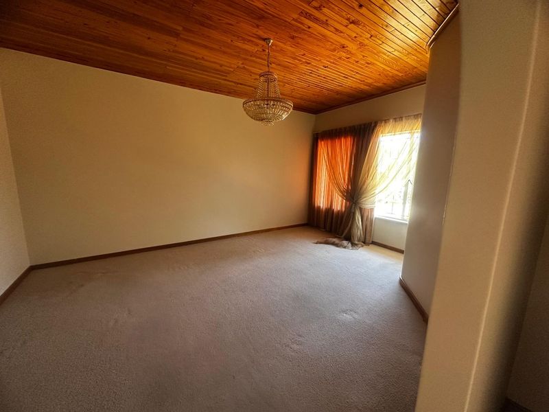 Spacious bedroom featuring a warm timber tongue and groove ceiling, fitted carpeting, and a classic crystal chandelier.