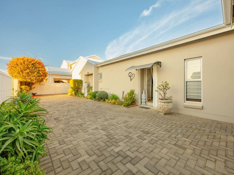 A well-maintained front exterior featuring a paved driveway, neutral facade, and a functional metal awning over the entrance.