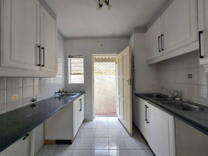 A functional scullery featuring white cabinetry, granite countertops, double stainless steel sinks, and tiled finishes with direct access to an outdoor area.