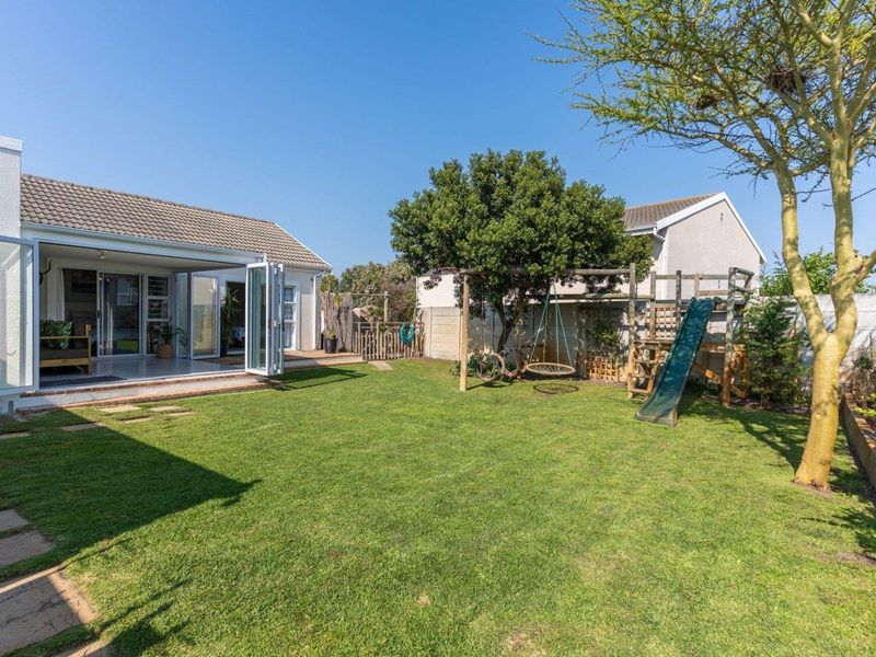 A well-maintained rear garden featuring a lawn, paved patio area, and bi-fold doors providing seamless indoor-outdoor flow to the main residence.