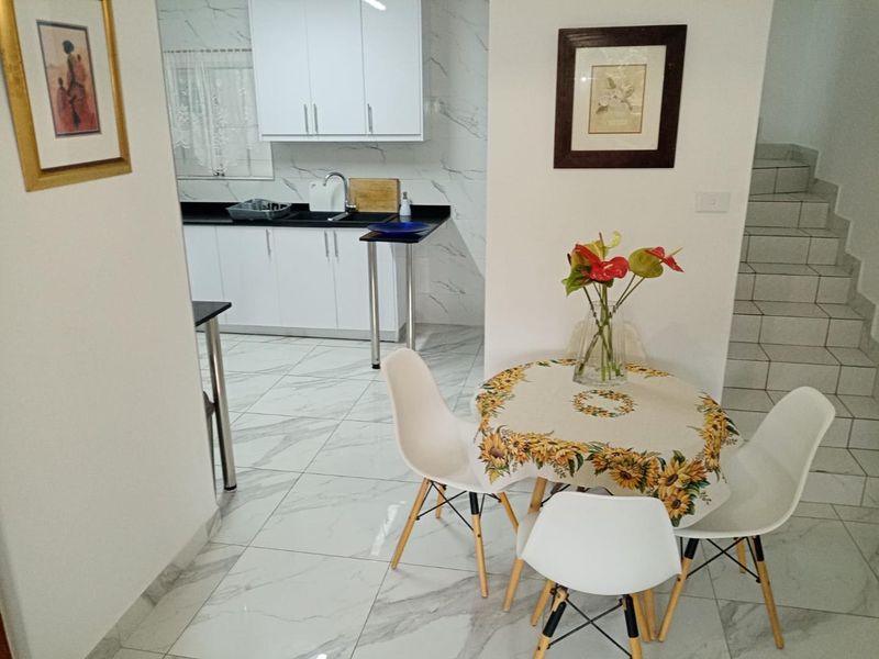 Open plan kitchen and dining area featuring modern marble-look floor tiles, white cabinetry with black countertops, and an adjacent tiled staircase.