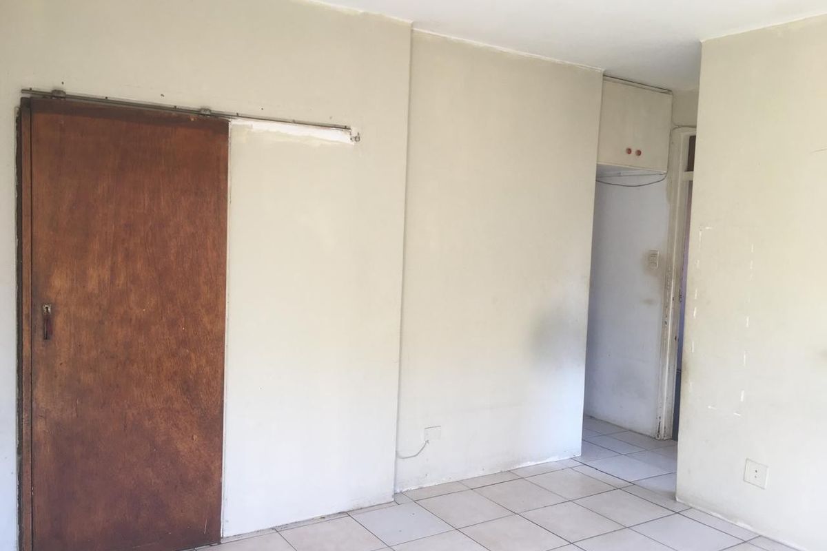 An empty living area featuring ceramic floor tiles, a sliding wooden door, and a built-in storage cupboard, requiring cosmetic updates and paint.