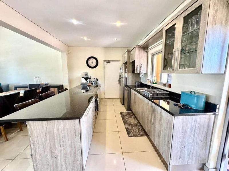 Modern kitchen featuring light wood-grain cabinetry, contrasting black granite countertops, a central island, and tiled flooring, seamlessly flowing into the adjacent dining area.