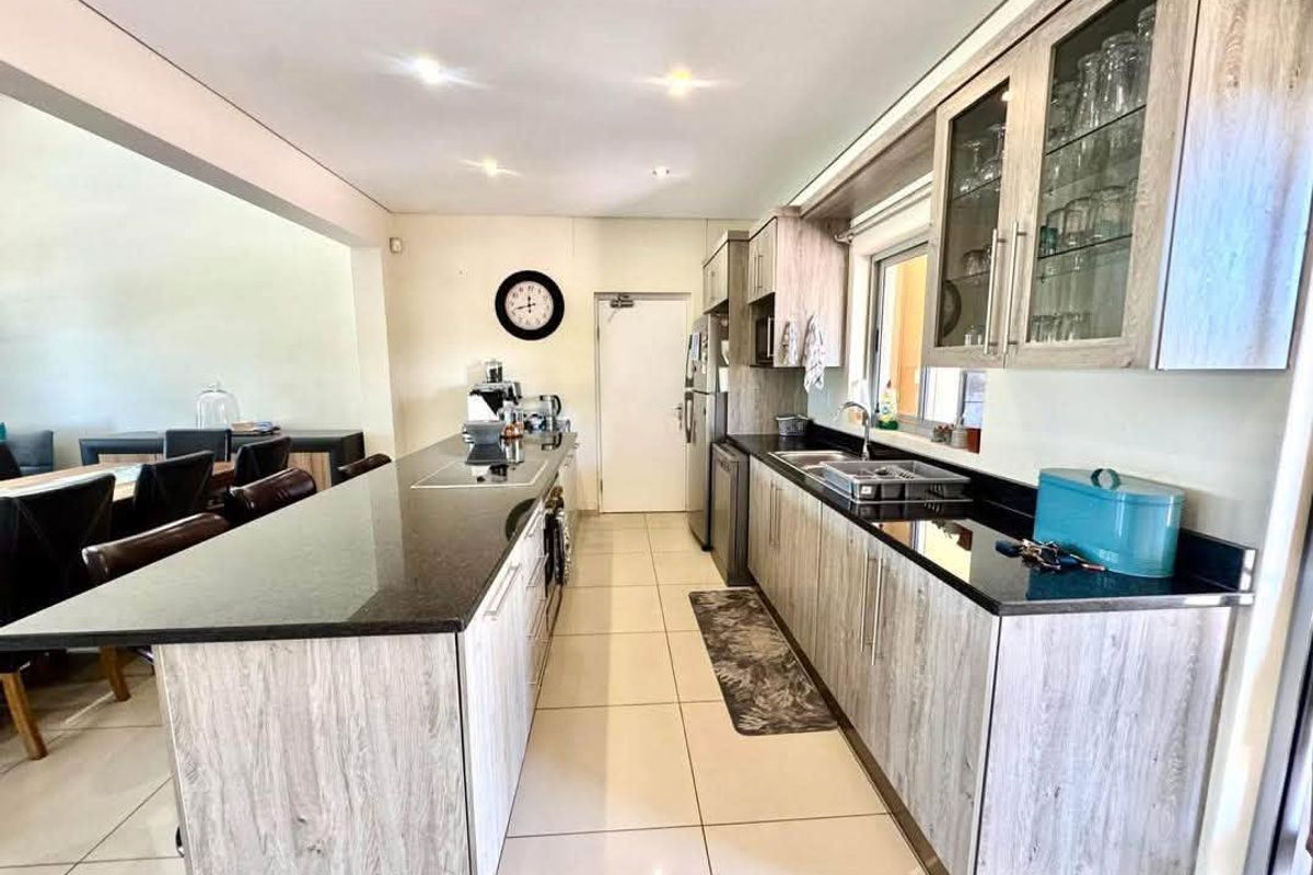 Modern kitchen featuring light wood-grain cabinetry, contrasting black granite countertops, a central island, and tiled flooring, seamlessly flowing into the adjacent dining area.