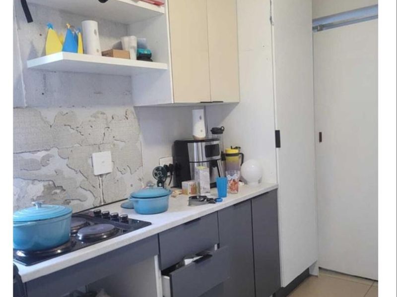 Compact kitchen featuring two-tone cabinetry, a built-in hob, and tiled flooring. The wall area requires finishing and plaster repair to complete the space.